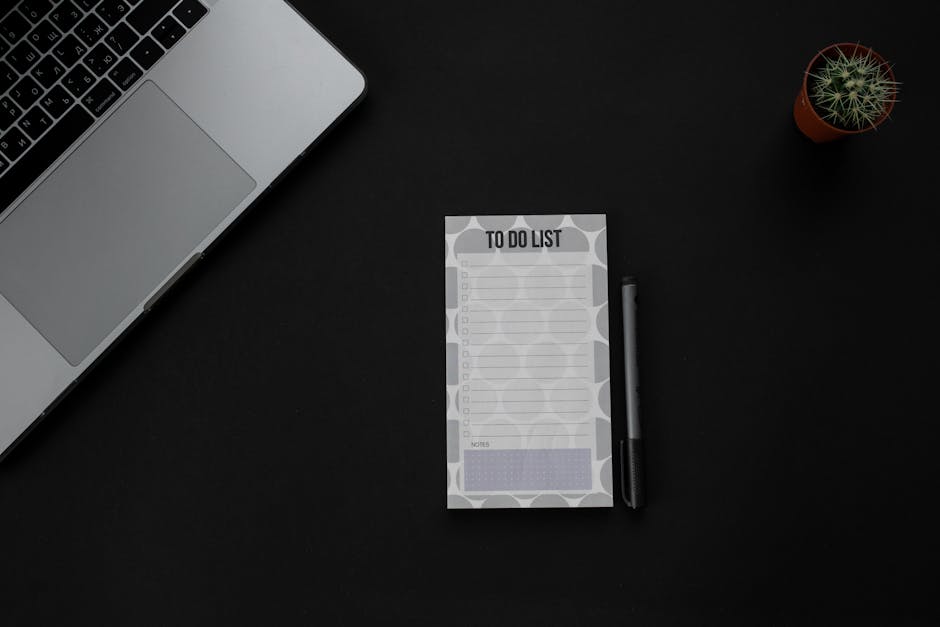 A minimalistic desk setup featuring a laptop, to-do list, and pen on a dark background. Ideal for productivity themes.